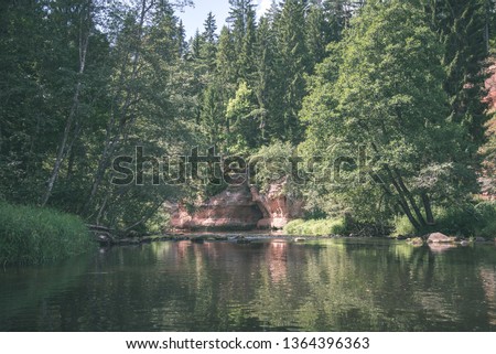 water stream in river of Amata in Latvia with sandstone cliffs, green foliage in summer morning - vintage retro film look