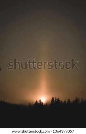 cold sunrise in winter forest with sun light pillar - an atmospheric optical phenomenon in which a vertical beam of light appears to extend above and/or below a light source - vintage retro look