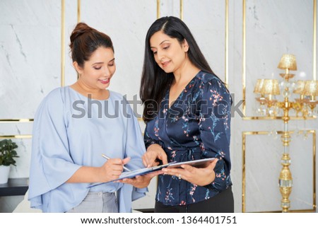 Two mature businesswomen standing in luxury hall and discussing business contract together