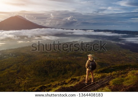 Man tourist looks at the sunrise on the volcano Batur on the island of Blai in Indonesia. Hiker man with backpack travel on top mountain, travel concept Royalty-Free Stock Photo #1364408183