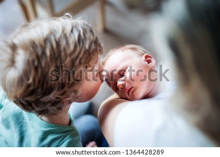 A small boy kissing a sleeping newborn baby brother at home.