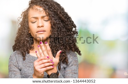 Young beautiful woman with curly hair wearing grey sweater Suffering pain on hands and fingers, arthritis inflammation