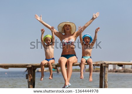 Happy mother with two sons twins sitting on the pier on the beach. Resort concept.