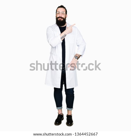 Doctor therapist man with long hair and bear wearing white coat cheerful with a smile of face pointing with hand and finger up to the side with happy and natural expression on face