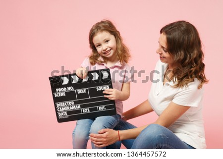 Woman in light clothes hold clapperboard, child baby girl. Mother, little kid daughter isolated on pastel pink wall background, studio portrait. Mother's Day, love family parenthood childhood concept