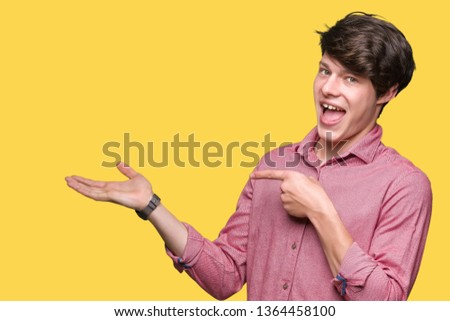Young handsome business man over isolated background amazed and smiling to the camera while presenting with hand and pointing with finger.