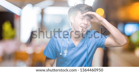 Young doctor wearing medical uniform over isolated background very happy and smiling looking far away with hand over head. Searching concept.