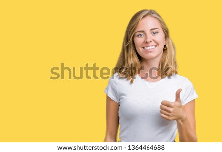 Beautiful young woman wearing casual white t-shirt over isolated background doing happy thumbs up gesture with hand. Approving expression looking at the camera showing success.