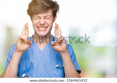 Young doctor wearing medical uniform over isolated background smiling crossing fingers with hope and eyes closed. Luck and superstitious concept.