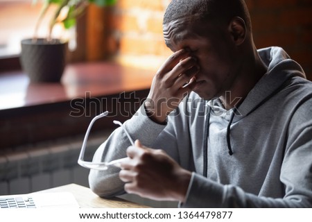 African student or worker sitting at table taking off eyeglasses massaging nose bridge suffering from dry eyes or eyestrain after long computer usage, modern tech negative impact on the health concept Royalty-Free Stock Photo #1364479877