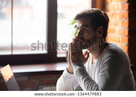 Young concerned businesswoman sitting at table near laptop folding hands together feels doubt unsure thinking making decision or waiting message good news having strong wish hope to get or win concept Royalty-Free Stock Photo #1364479883