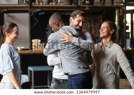 Different ethnicity multi racial guys hugging greeting each other best friends gathered in public place, spending Friday hanging out together, chance meeting, friendship between diverse people concept Royalty-Free Stock Photo #1364479997