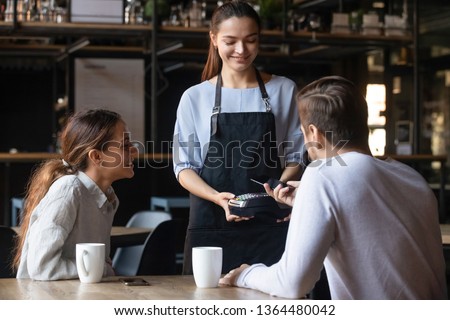 Diverse couple buyers male female pub bar client pay bill order use cellphone smartphone app near field communication system. Modern fast easy tech NFC contactless payment, food drink industry concept Royalty-Free Stock Photo #1364480042