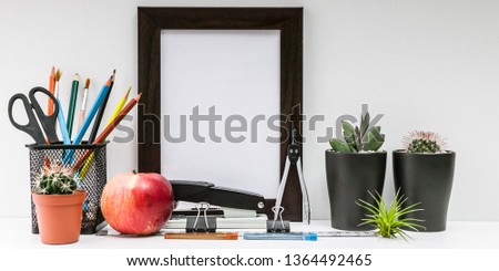 Empty dark photo frame, succulents in dark pots, colored pencils, office supplies, red apple on a white background. Desktop MockUp. Scandinavian style in the interior.