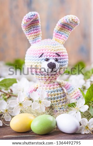 Crochet bunny on the background of delicate cherry flowers. Spring card. Easter concept. Knitted toy, handmade, needlework, amigurumi.