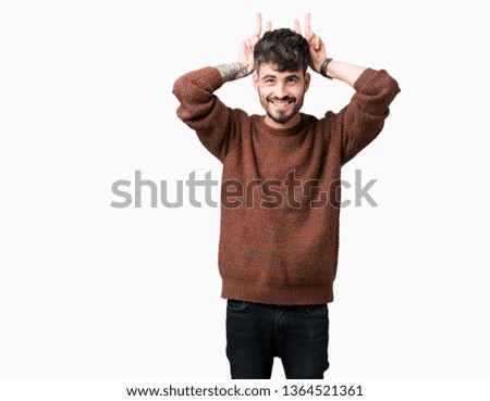 Young handsome man wearing winter sweater over isolated background Posing funny and crazy with fingers on head as bunny ears, smiling cheerful
