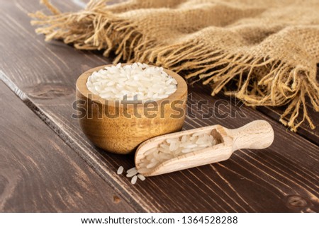 Lot of whole white jasmine rice grains in a wooden bowl with wooden scoop on jute cloth on brown wood Royalty-Free Stock Photo #1364528288