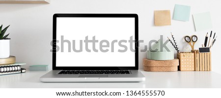 Panoramic photo of a stylish white, glossy desk with laptop mock up, boxes full of supplies, noteson the wall and notebooks.