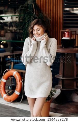 Young charming girl dressed in beige knit dress poses in the street