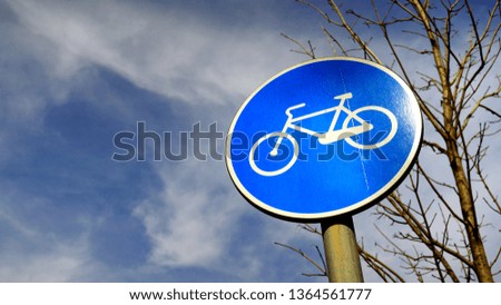 Round road sign indicating a bicycle lane with stylized bicycle on blue background, with cloudy sky