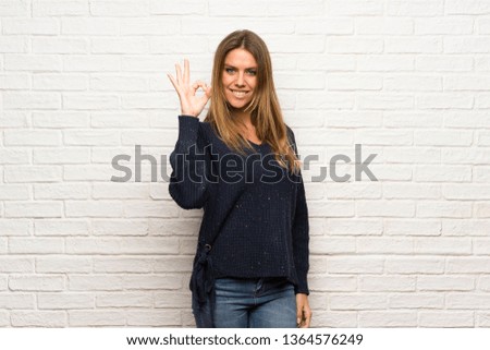 Blonde woman over brick wall showing ok sign with and giving a thumb up gesture