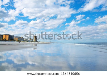 View of the ocean and beach, cloudy blue sky and hotels and buildings in the background.  Clouds reflected in the water on the beach, Jacksonville Florida, USA,