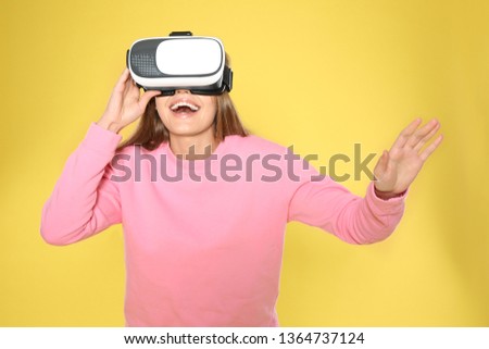 Emotional young woman playing video games with virtual reality headset on color background