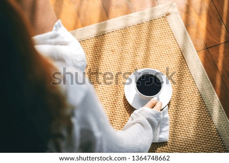 Top view image of a woman sitting and holding a cup of hot coffee on the floor in the morning