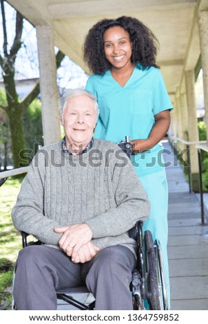 Aged senior man on the wheelchair assisted by african nurse in the garden patio.