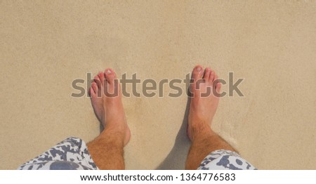 Feet stand on beach and sand with wave splash