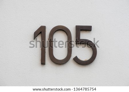 Vintage style house number 105. Weathered metal on white plastered wall.