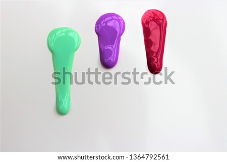Three drops of paint - light green, purple and red flow freely on a white background.