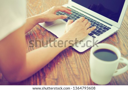 Work from home theme female hands using laptop on old dark wood texture with natural patterns table with blurred white cup with black coffee in foreground. Technology's impact on people's live concept