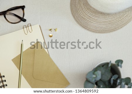 The golden opened notebook, pencil, paper clips, pins, envelope, spectacles and hat on the table