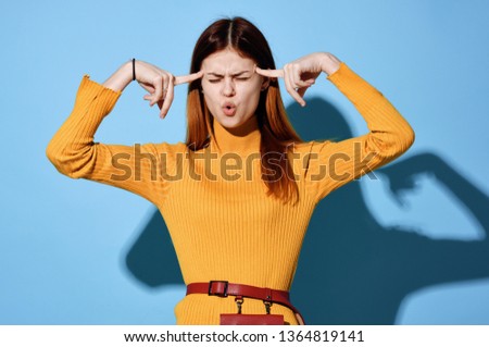 A woman in a yellow sweater touches her head with her fingers                               
