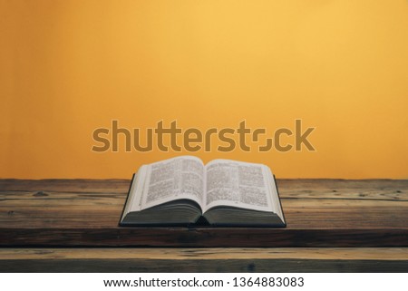 Open Holy Bible on a old oak wooden table. Orange wall background.	