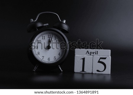 Wooden cube shape calendar for April 15 with black clock on black background. 