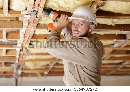 tradesman using drill on wooden framework of ceiling Royalty-Free Stock Photo #1364937272