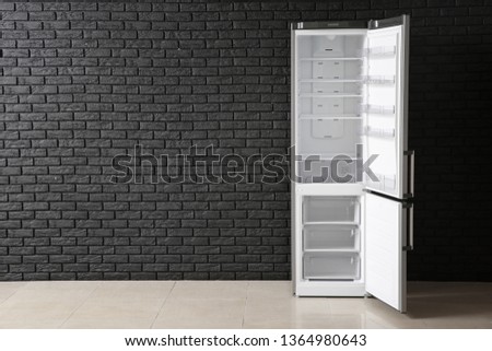 Open empty fridge near dark brick wall
