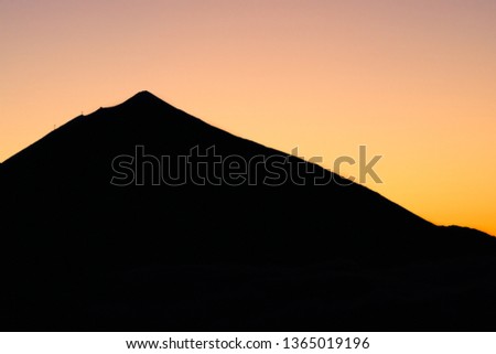 Contrast silhouette of volcano Teide in Tenerife, Canary Islands, Spain. Orange sunset sun in background and contour of mountain in foreground. Visible cable railway. Picture suitable for wallpaper.