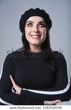 Smiling woman wearing beret hat looking up, over gray background