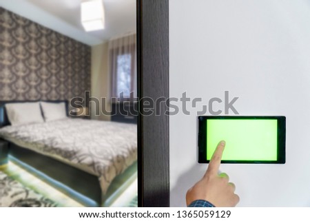 Smart home control and security concept. Device with blank screen hanging on a wall and person pressing button with his finger.