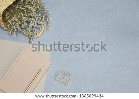 The Pink notebook, paper clips, straw basket with flowers on the blue desk