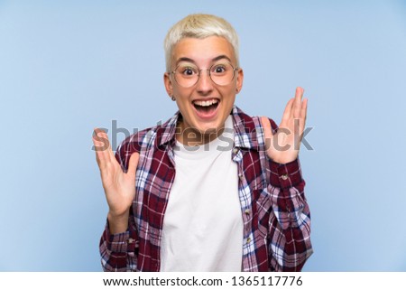Teenager girl with white short hair over blue wall with surprise facial expression