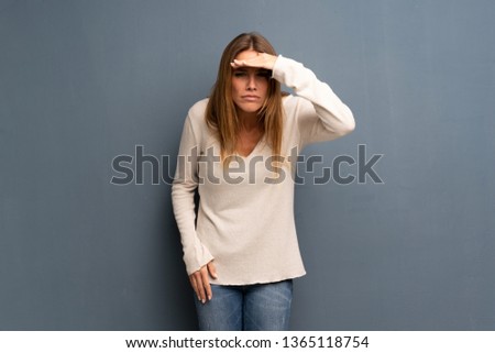 Blonde woman over grey background looking far away with hand to look something