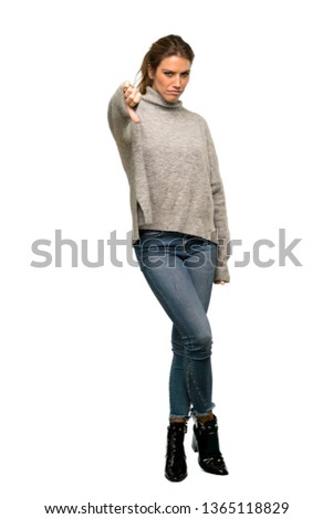 A full-length shot of a Blonde woman with turtleneck showing thumb down with negative expression over isolated white background