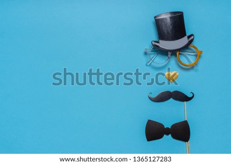 Various black photo booth props: cylinder hat, glasses, moustache, bow tie and nose in heart shape on blue background. Greeting card, text HAPPY FATHER'S DAY. Creative composition in minimal style