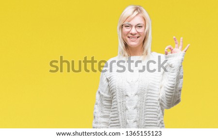 Young beautiful blonde woman wearing winter sweater and glasses over isolated background smiling positive doing ok sign with hand and fingers. Successful expression.