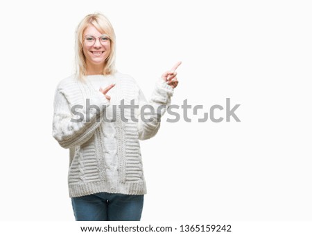 Young beautiful blonde woman wearing winter sweater and glasses over isolated background smiling and looking at the camera pointing with two hands and fingers to the side.