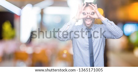 Young business man wearing glasses over isolated background doing ok gesture like binoculars sticking tongue out, eyes looking through fingers. Crazy expression.